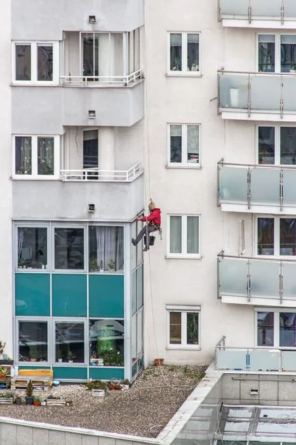 A worker cleaning skyscraper windows with a harness in an urban setting.